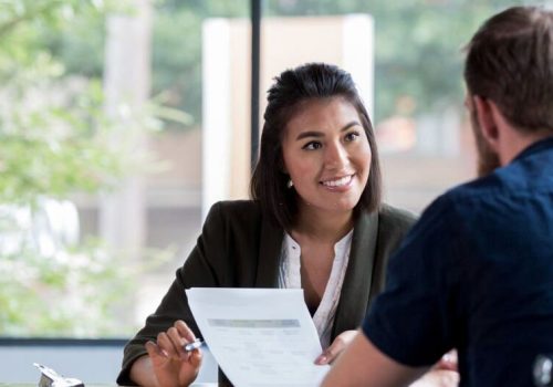 Hispanic businesswoman smiles while showing a document to a male associate.